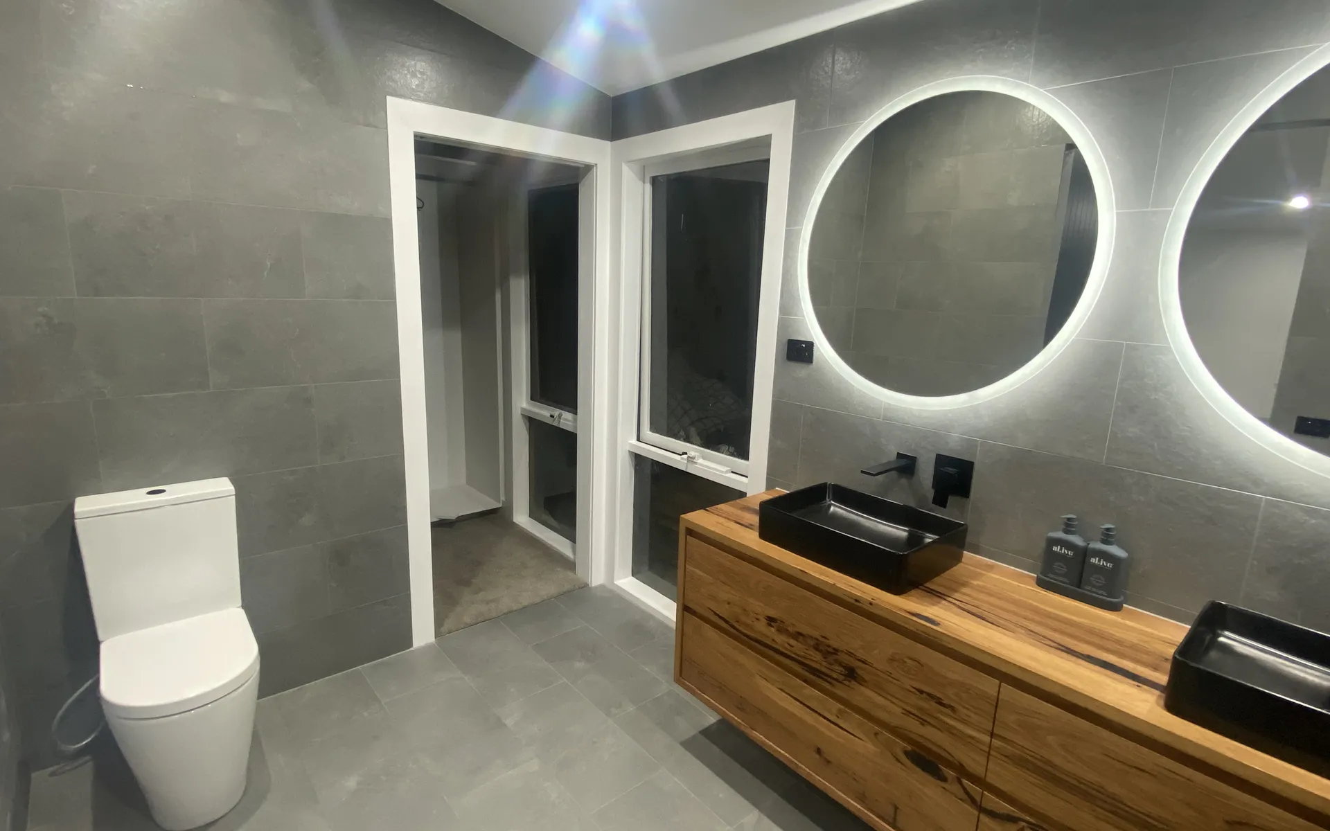 Renovated bathroom with grey tiling, timber vanity and backlit mirrors